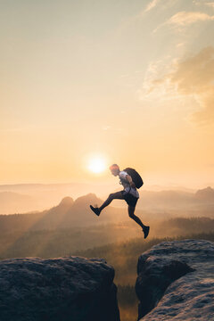 Side view of man with backpack jumping on cliff at sunset