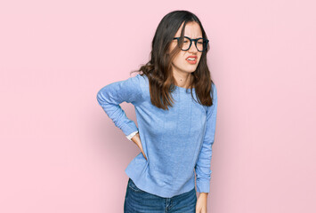 Young beautiful woman wearing casual clothes and glasses suffering of backache, touching back with hand, muscular pain