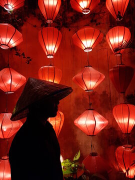 Silhouette of man wearing conical hat standing beside red lit lanterns