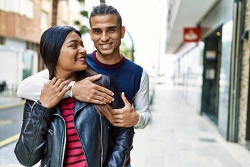 Young latin couple smiling happy and hugging walking at the street of city.