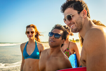 Obraz premium Smiling friends in sunglasses carrying bodyboards on beach