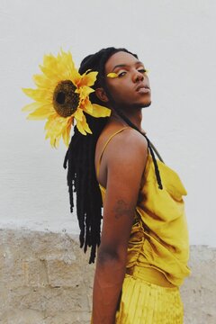 Trans woman posing in yellow dress with sunflower on their dreadlocks