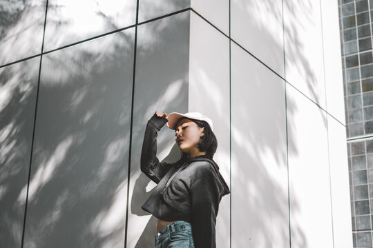 Woman in a dark sweater blue jeans and hat standing to a grid wall