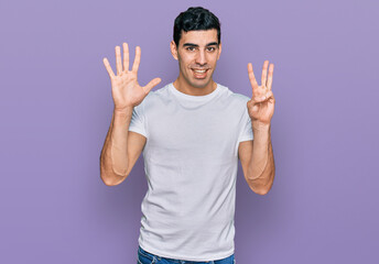 Handsome hispanic man wearing casual white t shirt showing and pointing up with fingers number eight while smiling confident and happy.
