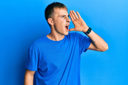 Young caucasian man wearing casual blue t shirt shouting and screaming loud to side with hand on mouth. communication concept.