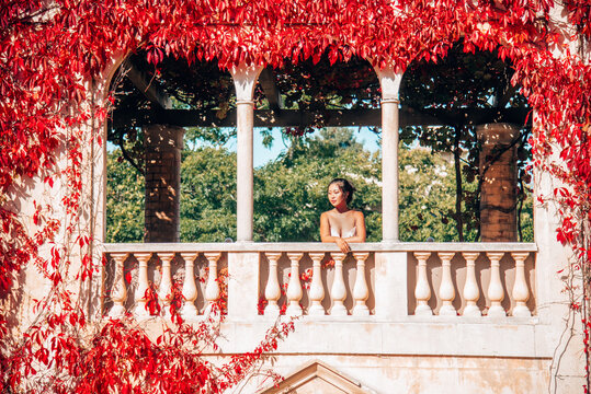 Woman standing on balcony overgrown with red ivy
