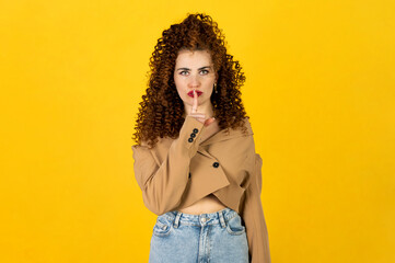 Woman with red curly hair in brown top and blue jeans against yellow background