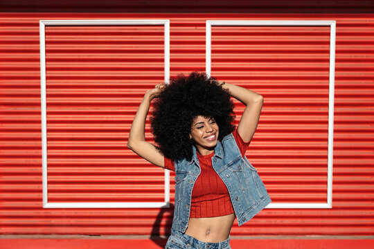 Young Black woman with Afro hair wearing denim vest with red shirt against red rolling shutters