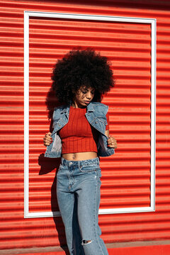 Young Black woman with Afro hair wearing denim vest with red shirt against red rolling shutters