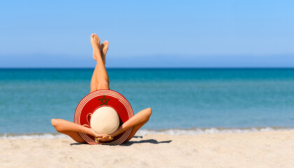 A slender girl on the beach in a straw hat in the colors of the Morocco flag. The concept of a perfect vacation in a resort in the Morocco. Focus on the hat.