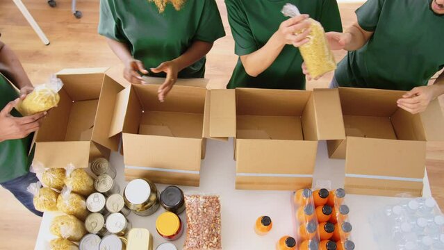 charity, donation and volunteering concept - international group of happy smiling volunteers packing food in boxes at distribution or refugee assistance center
