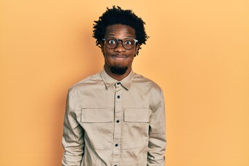 Obraz premium Young african american man wearing casual clothes and glasses puffing cheeks with funny face. mouth inflated with air, crazy expression.
