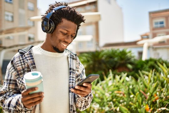 Handsome black man with afro hair wearing headphones listening to music using smartphone