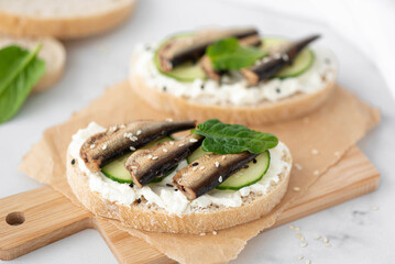 sandwich with sprats, curd cheese and cucumber on a wooden board
