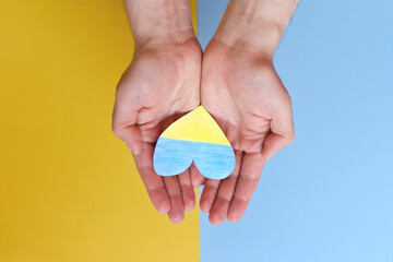 Top view of man hands holding Ukraine flag painted heart isolated on yellow, blue background. Concept symbol of help, support and no war in Ukraine