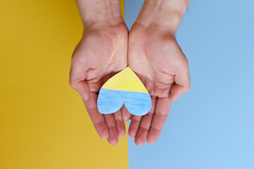 Top view of man hands holding Ukraine flag painted heart isolated on yellow, blue background. Concept symbol of help, support and no war in Ukraine