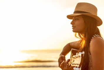 Indian woman wearing hat playing guitar on beach