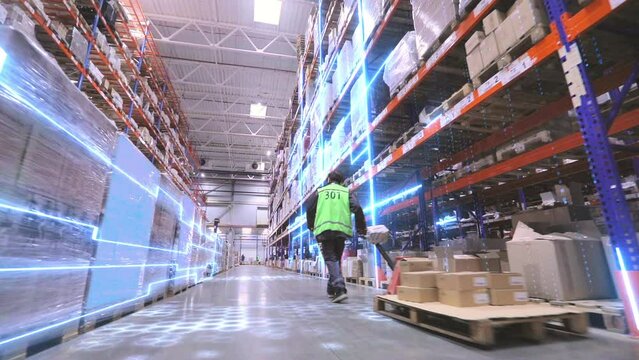 A worker is carrying a rokla through a large warehouse. The worker walks through the warehouse. Digitalization of production. Futuristic production concept.
