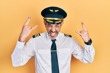 Handsome middle age man with grey hair wearing airplane pilot uniform shouting with crazy expression doing rock symbol with hands up. music star. heavy music concept.