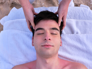 Fototapeta na wymiar A young man receiving a head massage on a beach in Valencia by a young chiromassage therapist.