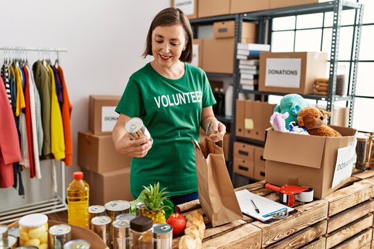 Middle age hispanic woman preparing bag with groceries at donations stand