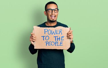 Young african american man holding power to the people banner winking looking at the camera with sexy expression, cheerful and happy face.