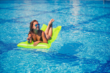 Young sexy wman in a swimsuit swims in the pool on an inflatable mattress. Girl in sunglasses in a blue pool on vacation