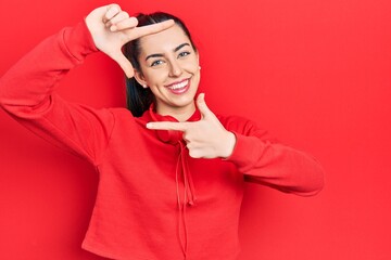 Beautiful woman with blue eyes wearing gym clothes and headphones smiling making frame with hands and fingers with happy face. creativity and photography concept.