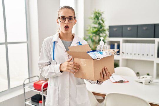 Young doctor woman holding box with medical items scared and amazed with open mouth for surprise, disbelief face