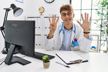 Young caucasian doctor man working at the clinic showing and pointing up with fingers number nine...