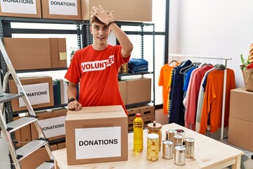 Young caucasian man volunteer holding donations box surprised with hand on head for mistake,...
