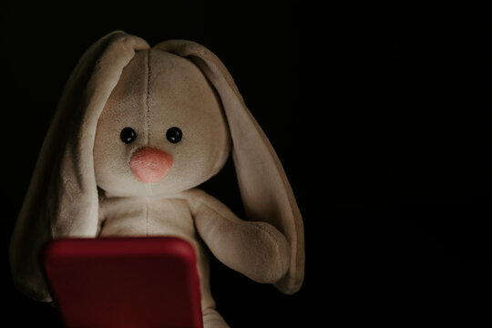Toy bunny with smartphone in bedroom close-up. Kid's addcition concept