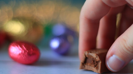 Plan rapproché d'une main qui tient un chocolat semi mangé sur un fond flou avec des œufs de...