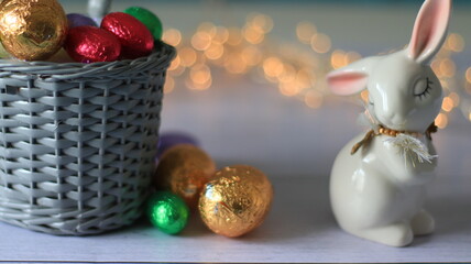 Plan rapproché d'un panier en osier avec des œufs de Pâque multicolors, un lapin de décoration et un fond flou lumineux.