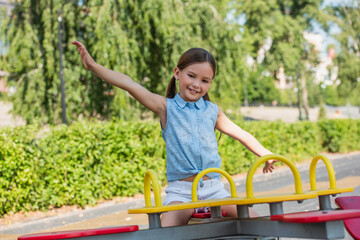 excited girl looking at camera while riding seesaw with outstretched hands.