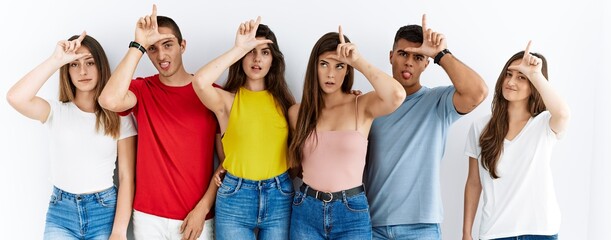 Group of people wearing casual clothes standing over isolated background making fun of people with fingers on forehead doing loser gesture mocking and insulting.