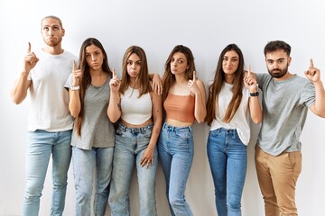 Obraz premium Group of young friends standing together over isolated background pointing up looking sad and upset, indicating direction with fingers, unhappy and depressed.