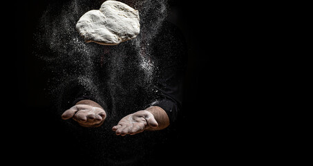 Fototapeta na wymiar flying pizza dough with flour scattering in a freeze motion of a cloud of flour midair on black. Cook hands kneading dough. copy space