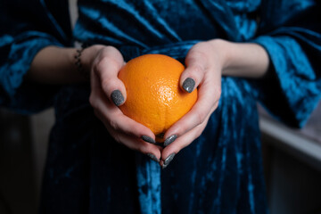 Fresh orange in woman hands on the blue background. High quality photo