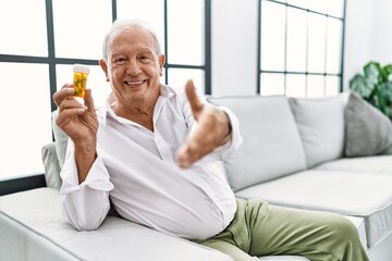 Senior man holding pills smiling friendly offering handshake as greeting and welcoming. successful business.