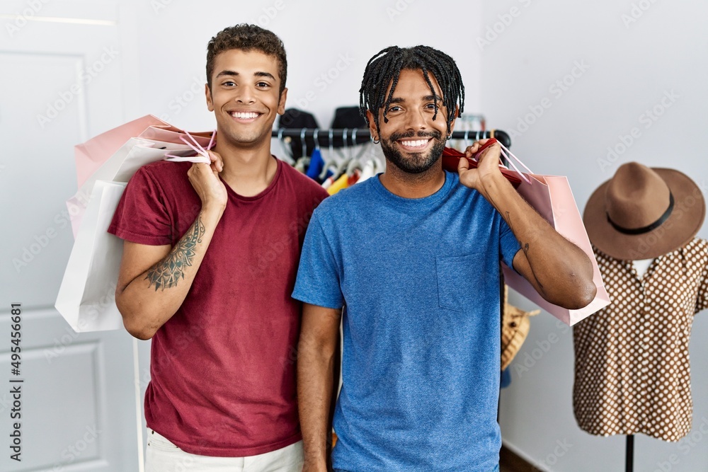 Canvas Prints Young hispanic men holding shopping bags at fashion boutique looking positive and happy standing and smiling with a confident smile showing teeth