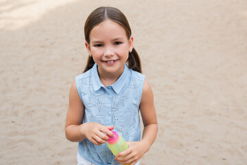 pleased girl with bubble blower smiling at camera outdoors.