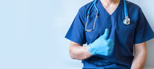 Cropped image of handsome male surgeon doctor with stethoscope in blue uniform with statoscope holding thumb up in clinic on blue background. banner with copy space - Powered by Adobe