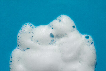 Foam on a blue background. Soapy liquid texture with bubbles. Natural sunshine and shadows. Skincare cleansing cosmetic in top view.