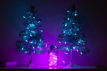 Two Christmas trees with bright neon lights. Copy space. Festive LED lighting