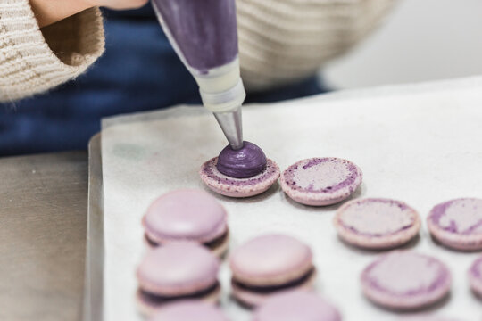 Unrecognizable pastry chef filling macaron with confectionery bag
