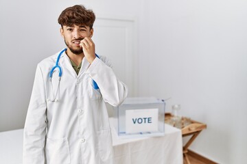 Young arab doctor man at political election by ballot looking stressed and nervous with hands on...