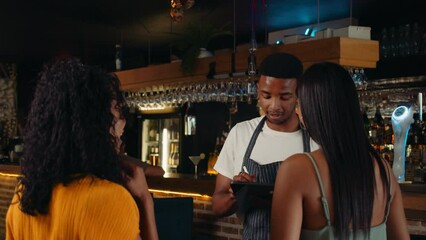 African American waiter greeting female customers at the door