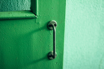 Old metal handle on a green door, green interior elements, vintage doorknob 