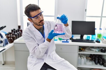 Young hispanic man wearing scientist uniform holding test tube at laboratory
